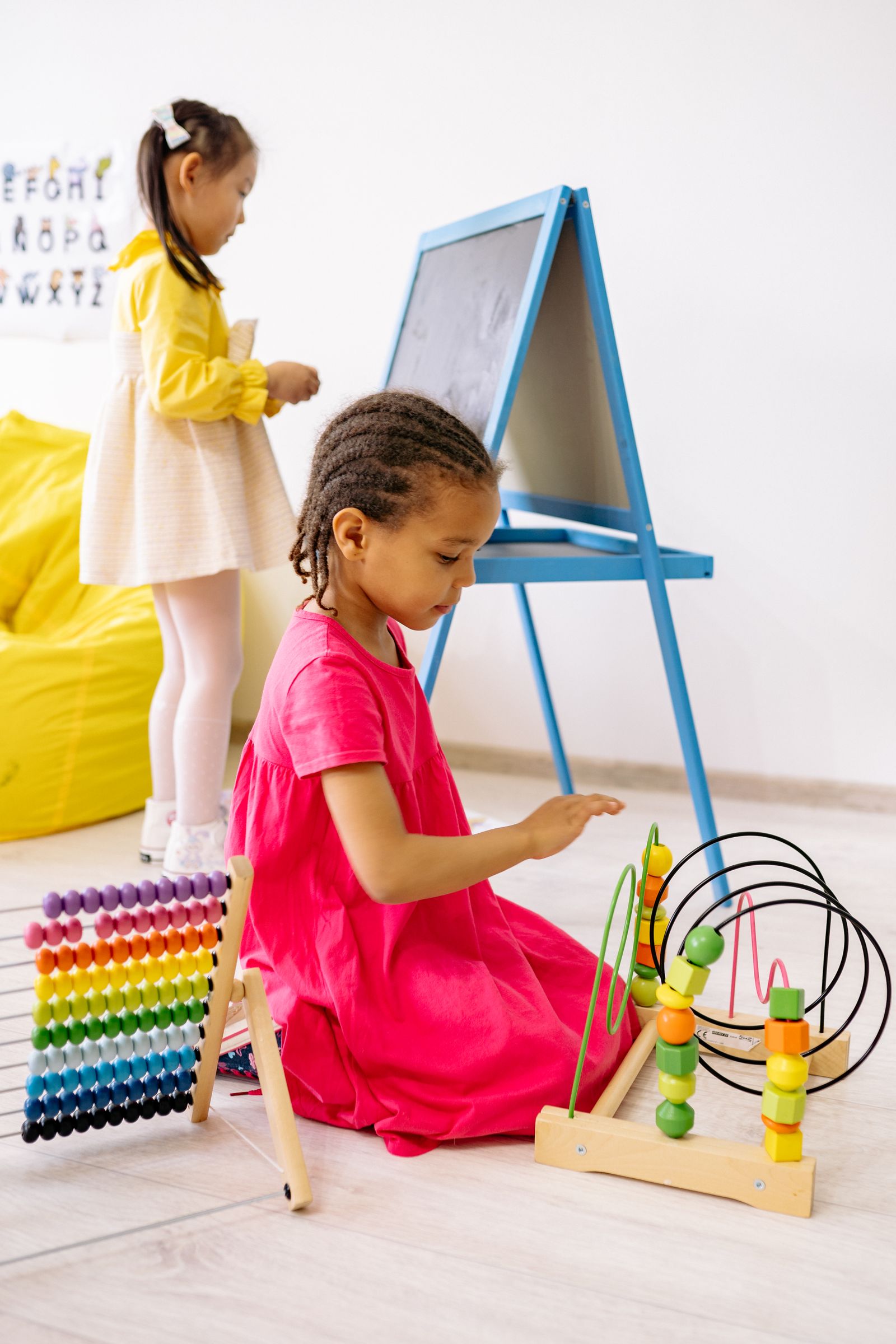 Two girls engaging in playful learning with abacus and toys in a bright classroom
