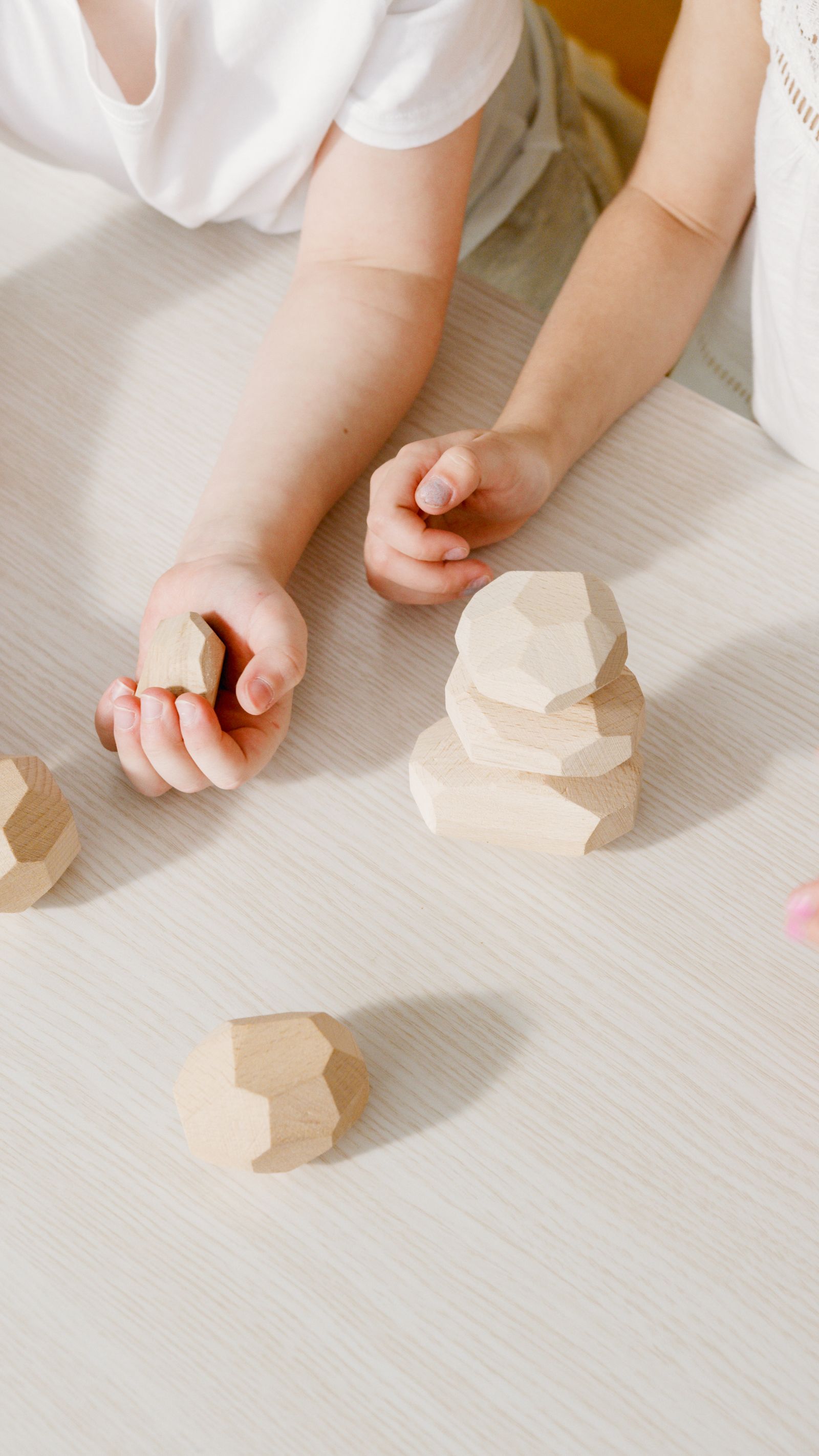 Close-up of kids' hands stacking geometric wooden blocks on a table
